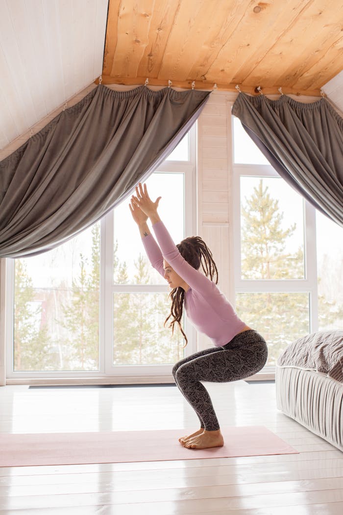 Woman doing yoga exercises indoors in a bright sunlit room with large windows.